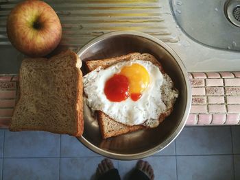 Low section of person standing by fried egg with breads in kitchen