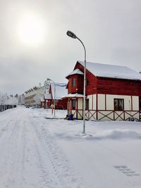 Snow covered road by houses against sky