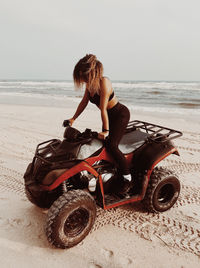 Woman sitting on sand at beach against clear sky