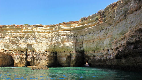 Rock formations by sea against clear blue sky