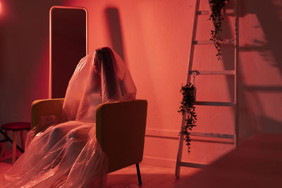 Woman sitting on armchair covered with plastic at home during pandemic