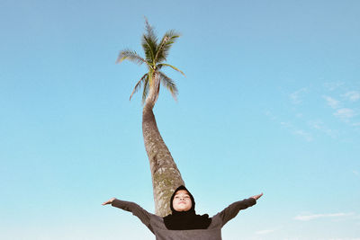 Low angle view of teenage girl with arms outstretched standing against blue sky