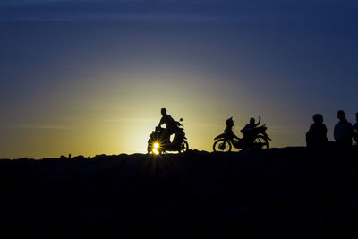 Silhouette people riding motorcycle against sky during sunset