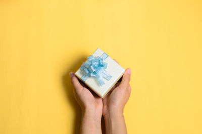 Cropped hands of woman holding gift box over yellow background