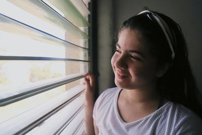 Close-up of smiling girl looking through window at home