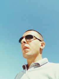 Low angle view of young man wearing sunglasses standing against clear sky