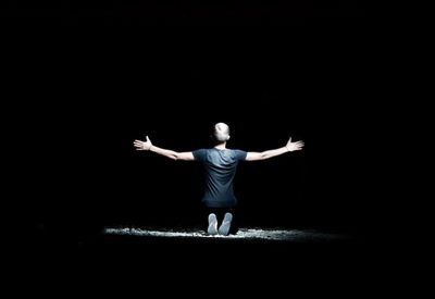 Rear view of man with arms outstretched standing against black background