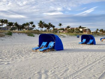 Deck chairs on sand at beach against sky