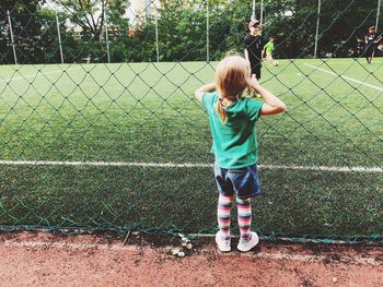 Rear view of girl looking at boys playing soccer on field