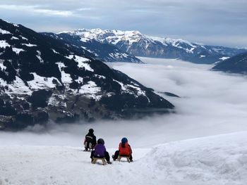 Rear view of friends on tobogganing on snowcapped mountain