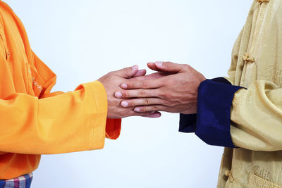 Midsection of friends wearing traditional clothing while holding hands against white background