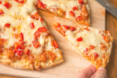 Cropped hand of person holding pizza on cutting board