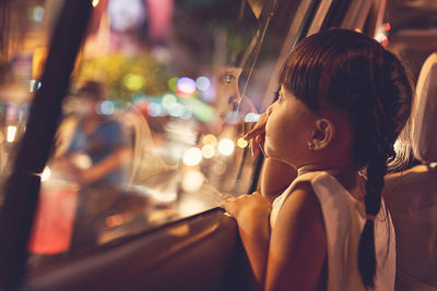 Close-up of cute girl looking through car window at night