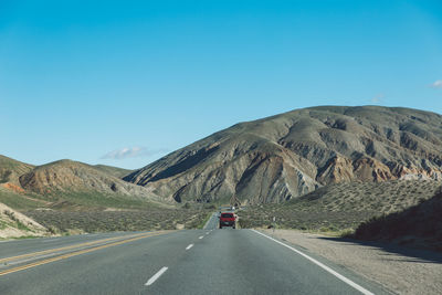 Vehicles on road by mountain against clear blue sky