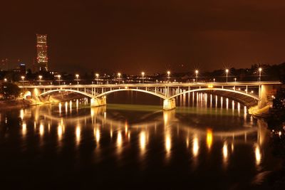 Illuminated bridge over river against sky in city at night