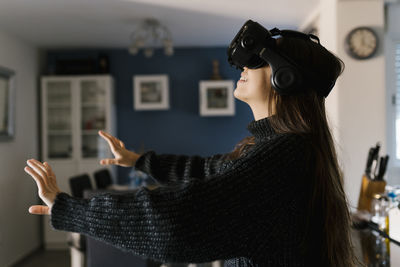 Playful teenage girl wearing virtual reality simulator eyeglasses sitting at home