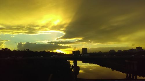 Silhouette factory against sky during sunset