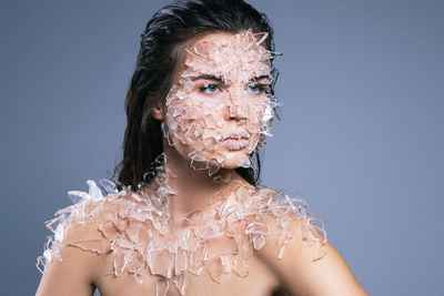 Close-up of woman with broken glass on body looking away against purple background