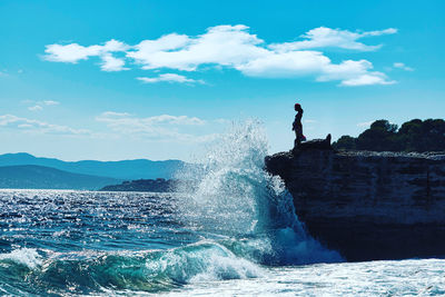 Water splashing on rocks by sea against sky