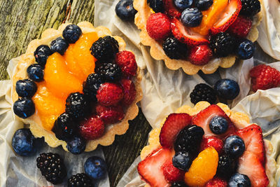 Glazed fruit tarts with raw blueberries, red and black raspberries, strawberries and orange sections