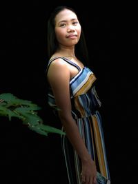 Portrait of smiling woman standing against black background