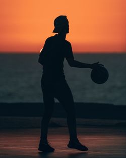 Silhouette man playing basketball during sunset