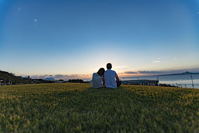 Rear view of man sitting on field against clear sky