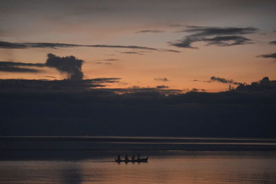 Silhouette people on sea against sky during sunset