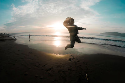 Man jumping at beach against sky during sunset