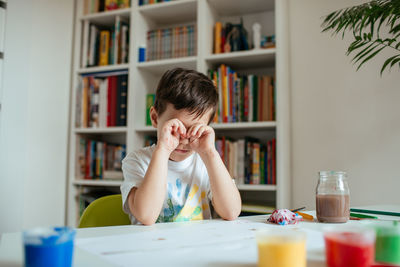 Tired boy sitting by table at home
