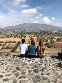 Rear view of people sitting on mountain against cloudy sky