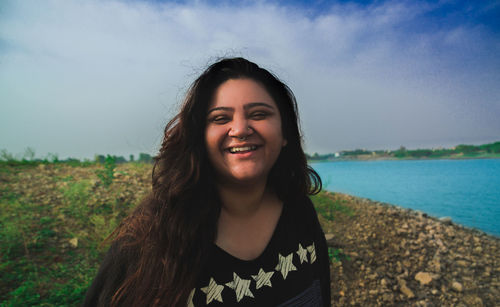 Portrait of smiling young woman standing on land against sky