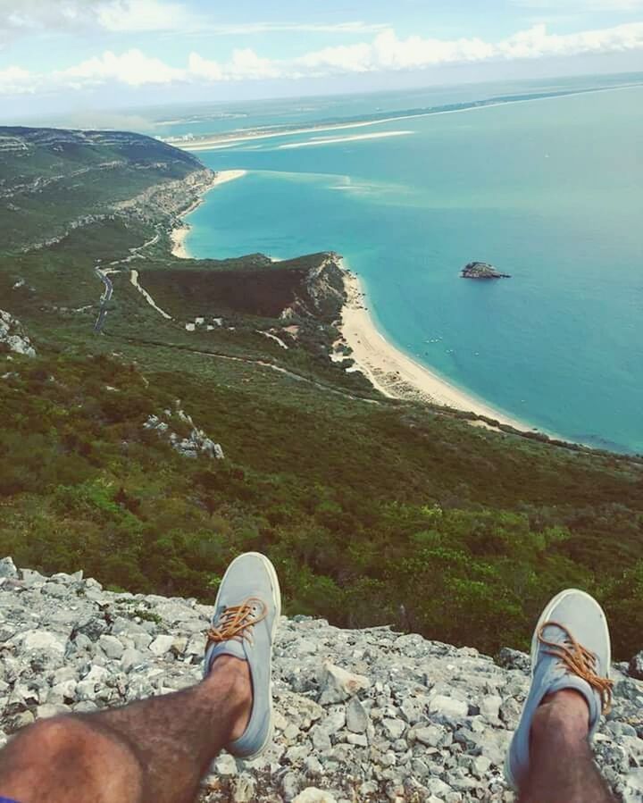 personal perspective, low section, human leg, shoe, real people, water, nature, day, sea, rock - object, high angle view, scenics, mountain, men, cloud - sky, standing, sky, lifestyles, leisure activity, beauty in nature, outdoors, landscape, cliff, adventure, beach, human body part, pebble beach, people