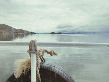 Rope tied to wooden post in sea against sky