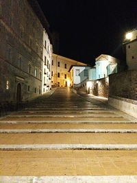 Walkway amidst illuminated buildings against sky at night