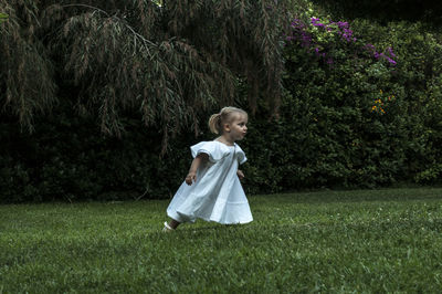 Cute girl running on grassy field against trees