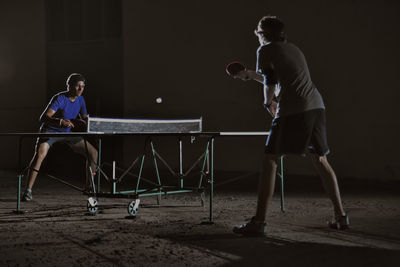 Friends playing table tennis against building at night