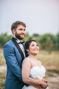 Smiling newlywed couple embracing on field