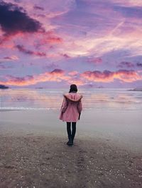 Rear view of woman standing on sand during sunset