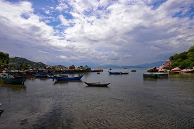 Boats moored in sea against cloudy sky