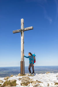 Germany, bavaria, female hiker standing in front of summit cross on hochries mountain