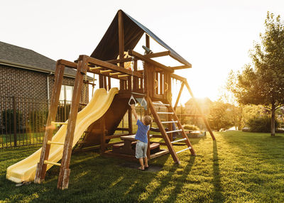 Boy playing with jungle gym in backyard during sunset