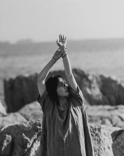 Young woman standing on rock formation against sky