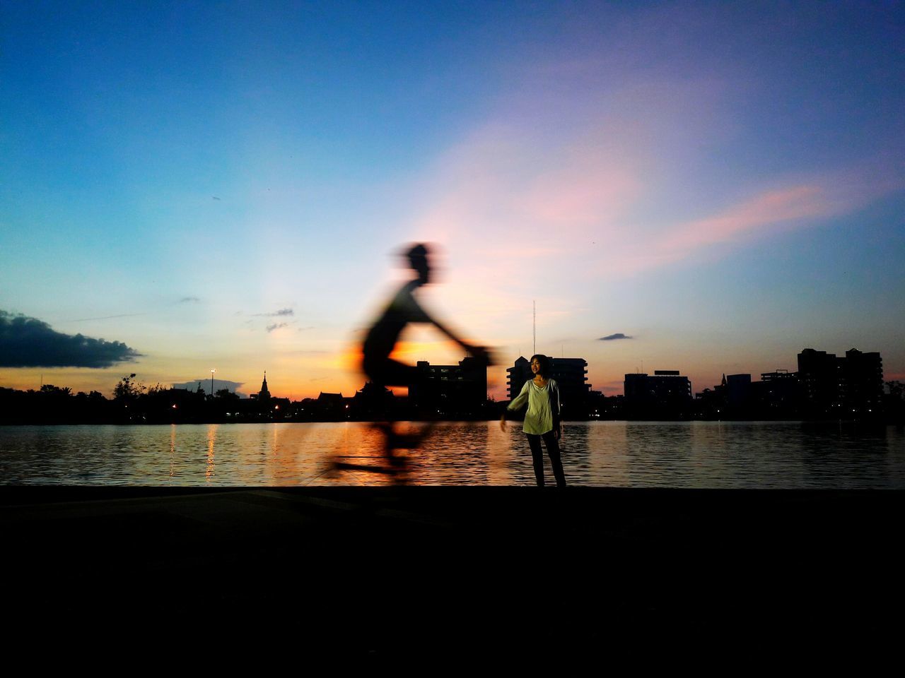 water, silhouette, building exterior, river, built structure, architecture, sky, riverbank, cloud, city, sunset, illuminated, moody sky, outdoors, city life, cloud - sky, bridge, no people, waterfront