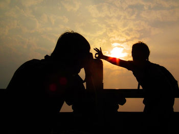 Silhouette people sitting against sky during sunset