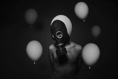 Man wearing gas mask by balloons against black background