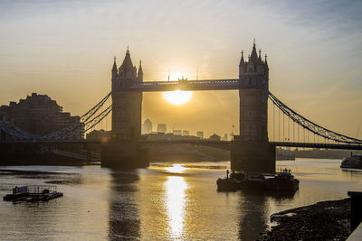 Bridge over river in city against sunset sky