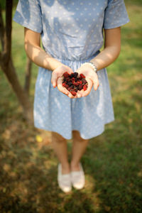 Low section of woman holding berries while standing in lawn