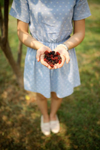 Midsection of woman holding strawberry while standing on field