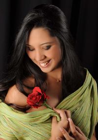 Smiling woman holding rose while standing against black background